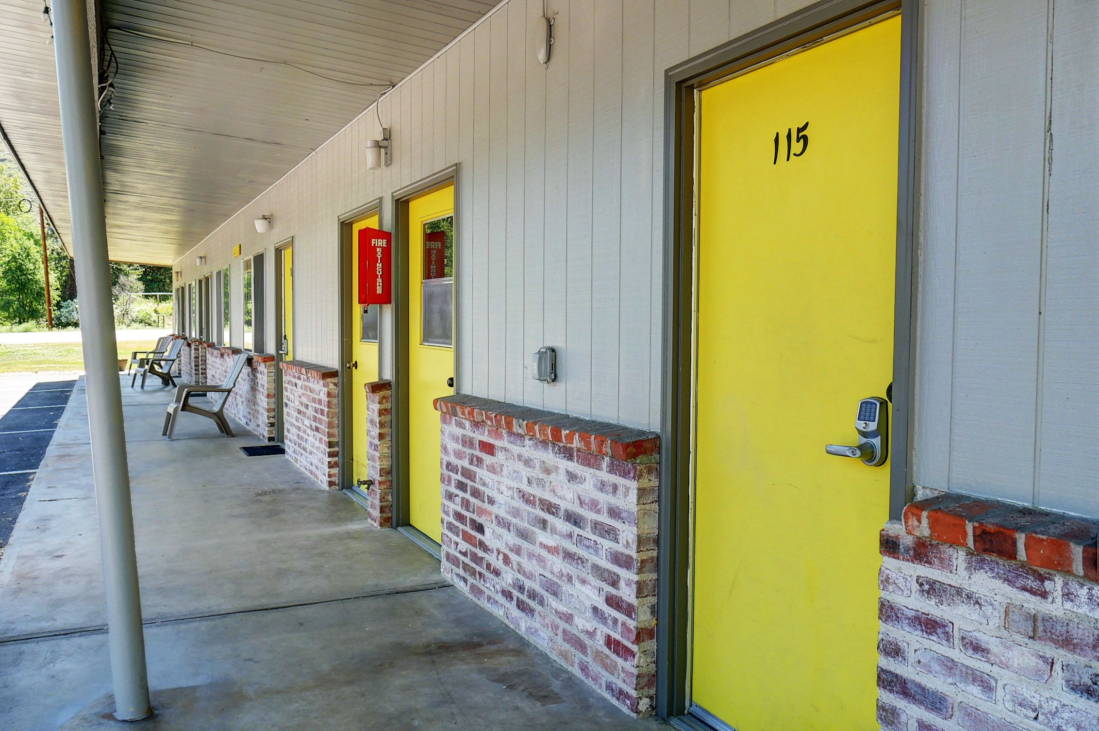 A row of yellow doors with a brick base, numbered 115, and a red fire exit sign.