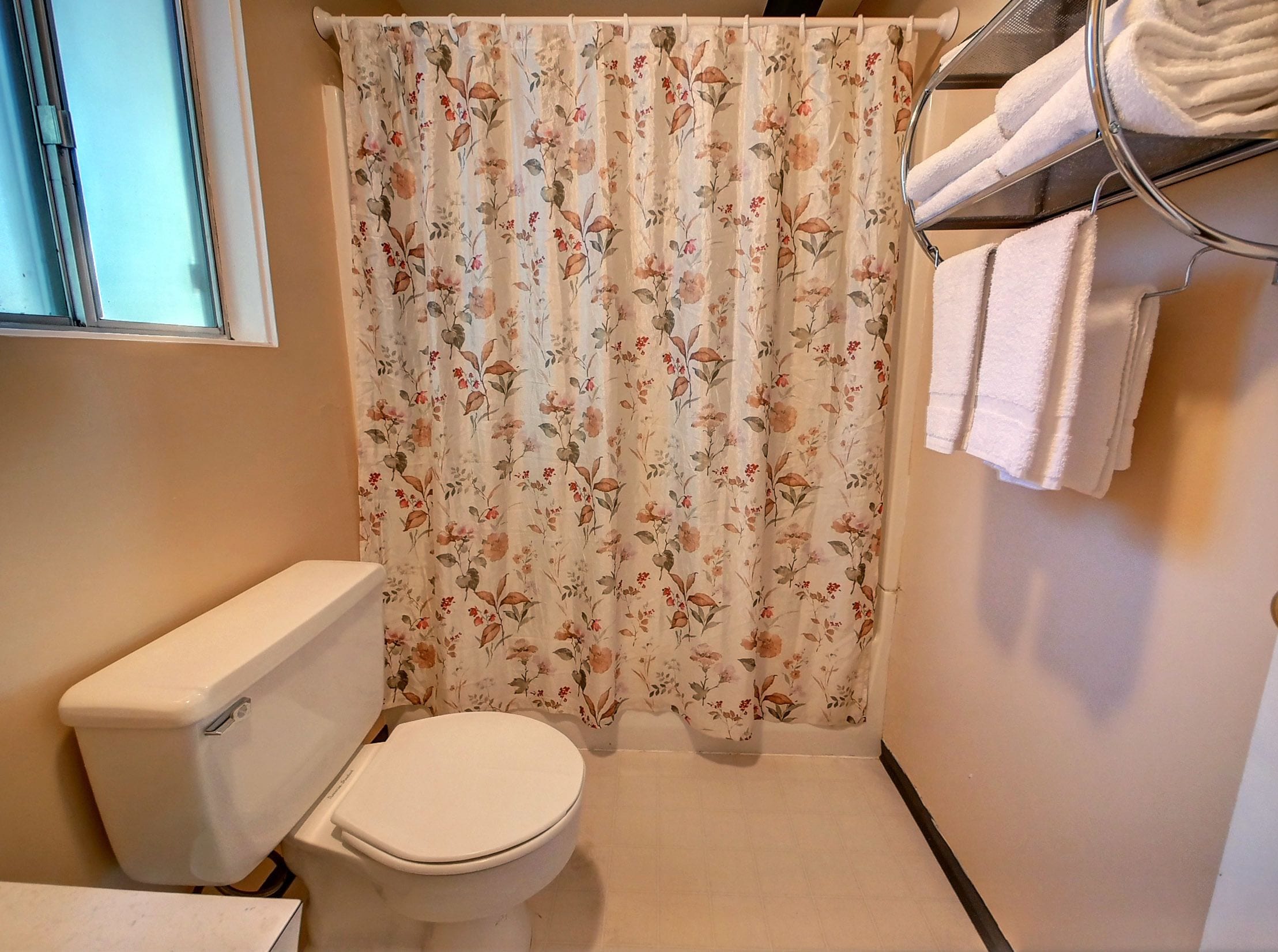 A bathroom with a toilet, a shower curtain with a floral pattern, and a towel rack with towels.