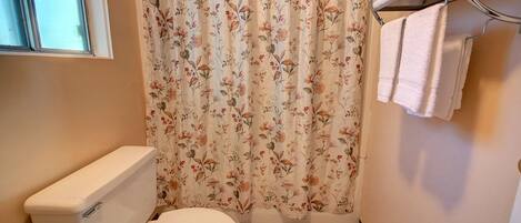 Un baño con inodoro, cortina de ducha estampada con motivos florales y toallero con toallas.