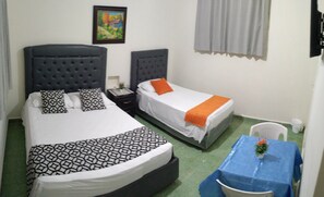 A hotel room with two beds, each with a headboard, a small table with a blue tablecloth, and a window with curtains. - Hostal Arboleda (Santo Domingo)