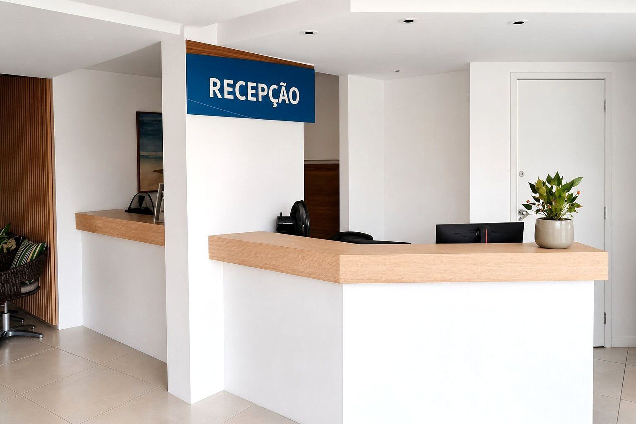 Balcão de recepção com placa indicando 'RECEPCAO', uma cadeira de escritório preta, um vaso de planta e uma porta ao fundo.