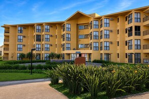 Un immeuble résidentiel à plusieurs étages, doté de balcons, de climatiseurs et d’un espace jardin aménagé.