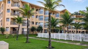 Ein mehrstöckiges Hotel mit Balkonen, Palmen und einem weißen Zaun.