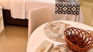 Ein Hotelzimmer mit einem ordentlich bezogenen Bett, einem runden Tisch mit Unterlage und einer Mandelkörbchen, sowie einer gemusterten Tischläufer.