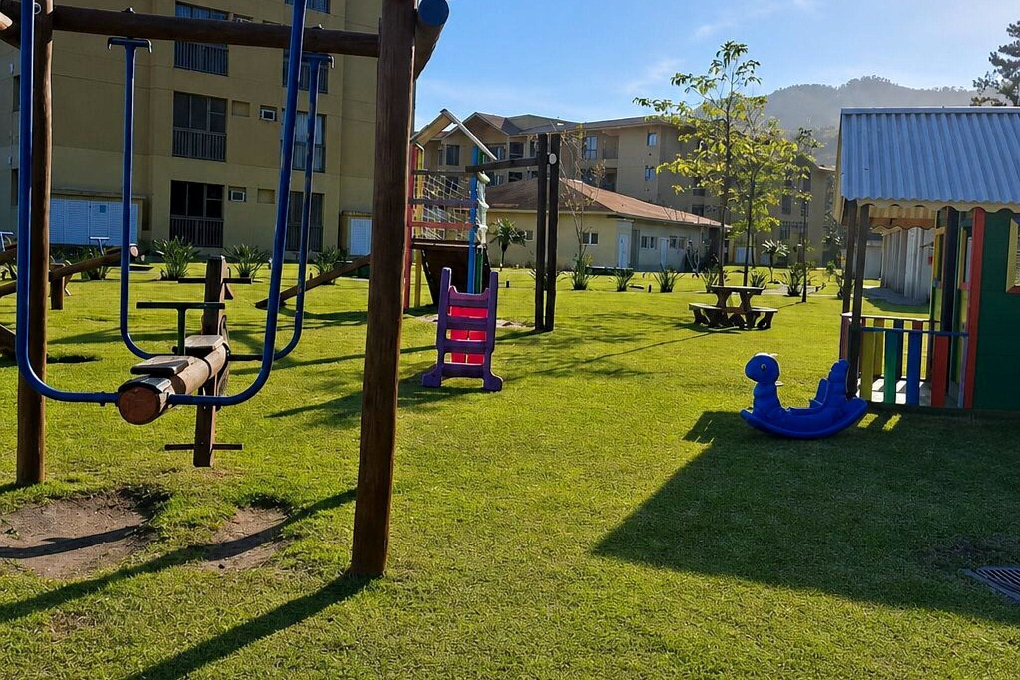 Un parque infantil con varios juegos, una mesa de picnic y un edificio al fondo.