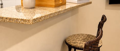 Uma bancada de cozinha com um vaso, uma caixa de madeira e um livro. Debaixo da bancada, dois cadeiras com tecido estampado.