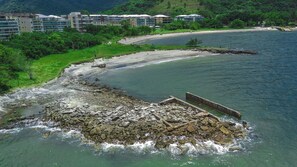 Un hotel frente al mar con costa rocosa, una playa de arena y vistas a un paisaje montañoso.