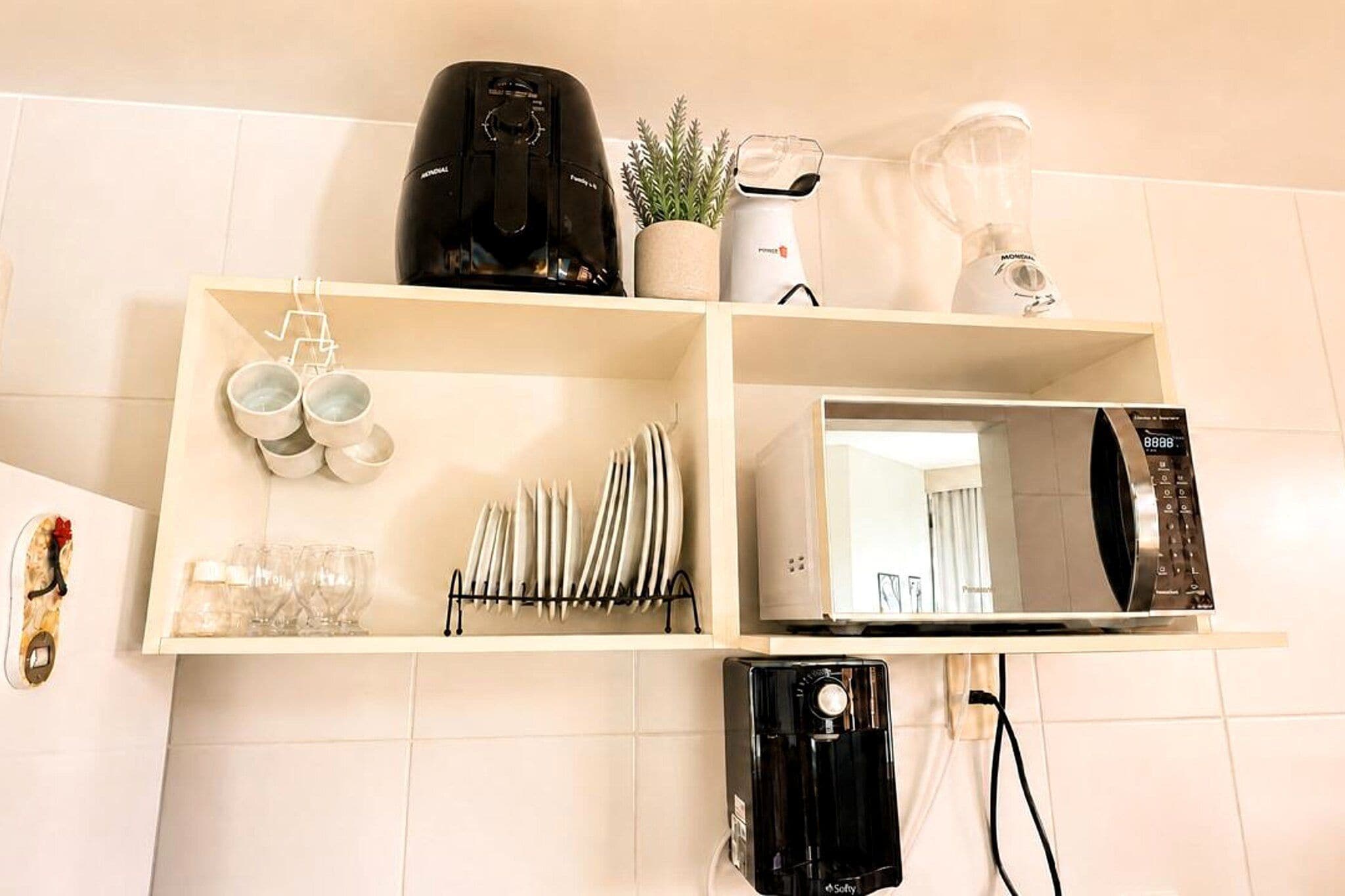 Cozinha com máquina de café, liquidificador, chaleira e micro-ondas em uma prateleira.