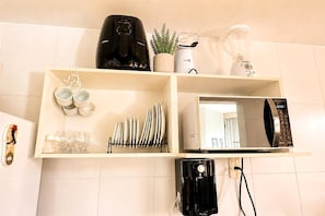 Una cocina con cafetera, licuadora, hervidor y microondas sobre una estantería.