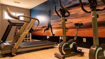 Academia com esteiras, elípticos e bicicletas ergométricas, com um mural de pôr do sol na parede.