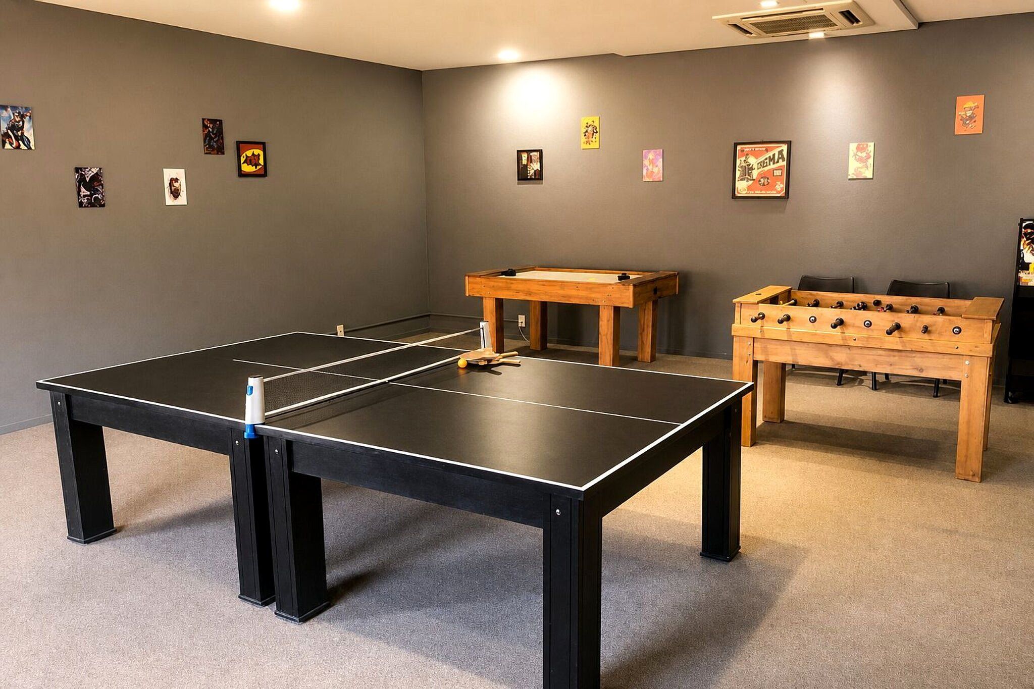Um quarto com mesa de pingue-pongue, mesa de futebol de mesa e diversos cartazes nas paredes.