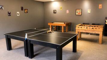 Um quarto com mesa de pingue-pongue, mesa de futebol de mesa e diversos cartazes nas paredes.