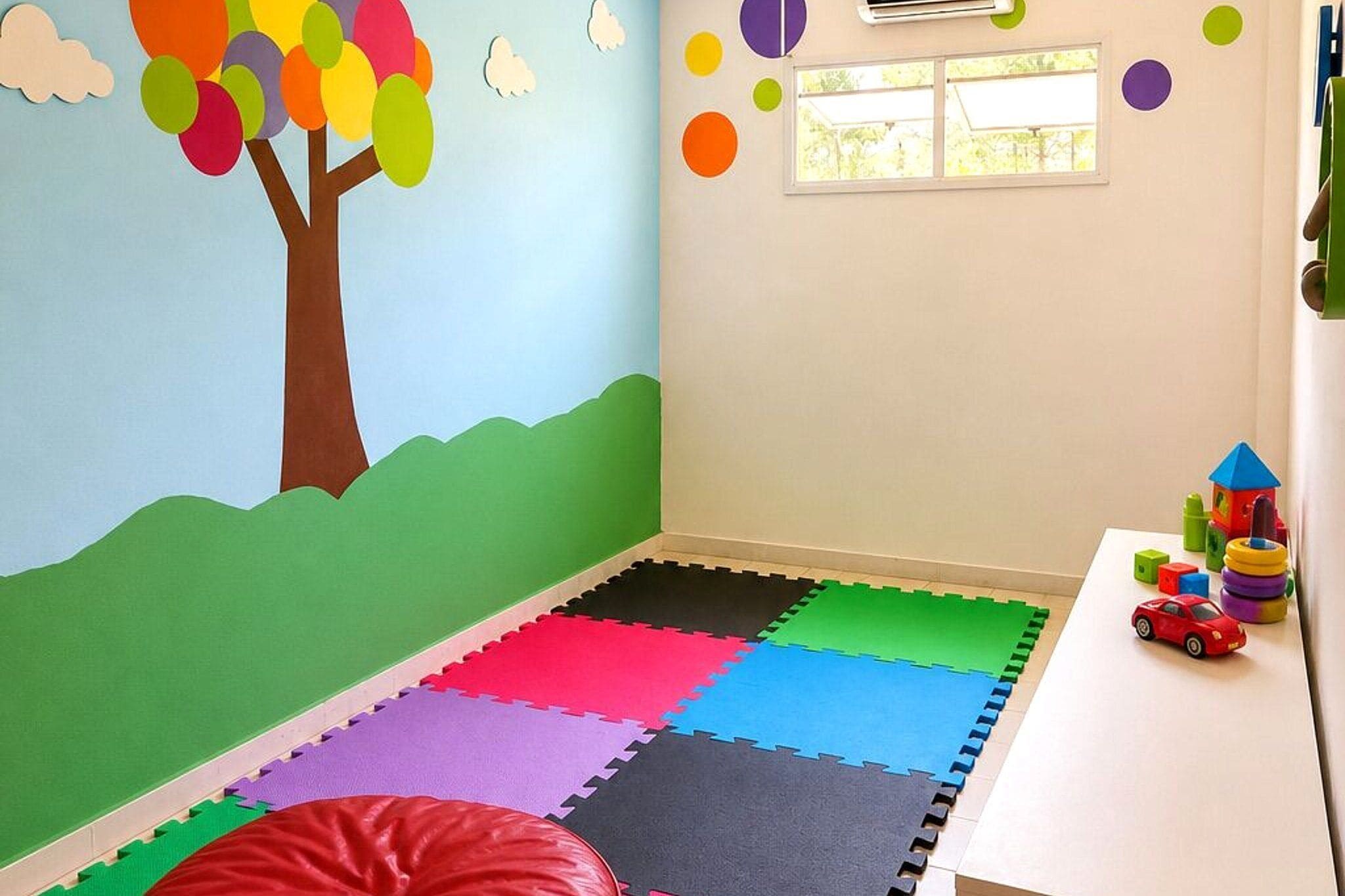 Ein Spielzimmer mit farbenfrohem Wandbild, einem Fenster und einer Spielmatte.