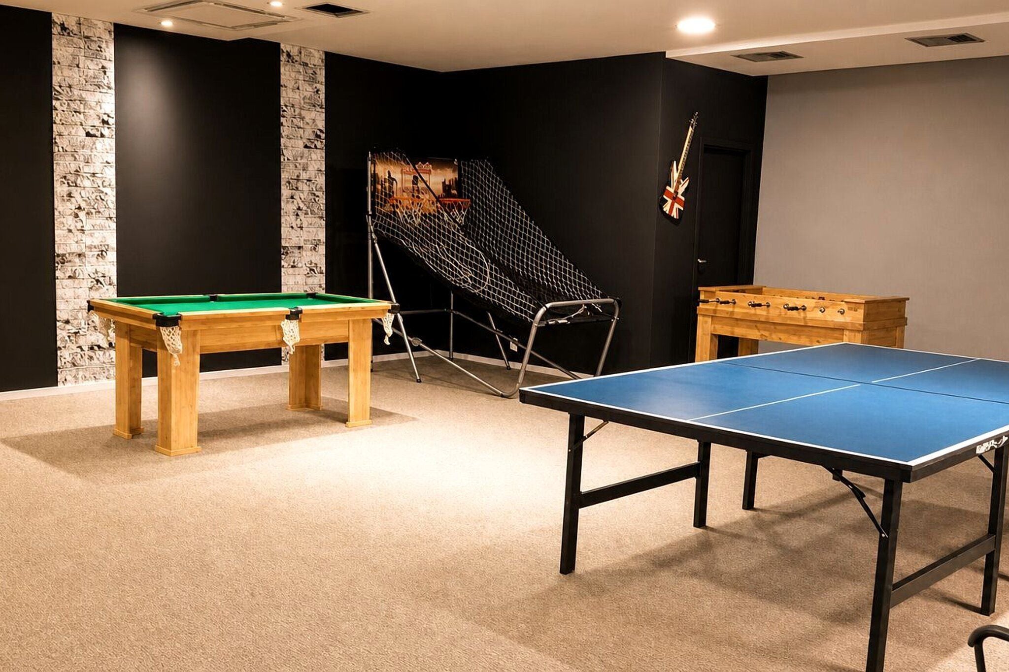 Quarto com mesa de bilhar, mesa de pingue-pongue e área de estar com uma poltrona.
