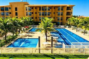 Et hotel med flere swimmingpools, palmer og en klar blå himmel.