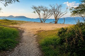A dirt path leading to a beach with trees and mountains in the background. - Reserva do Sahy, Condado (Mangaratiba)