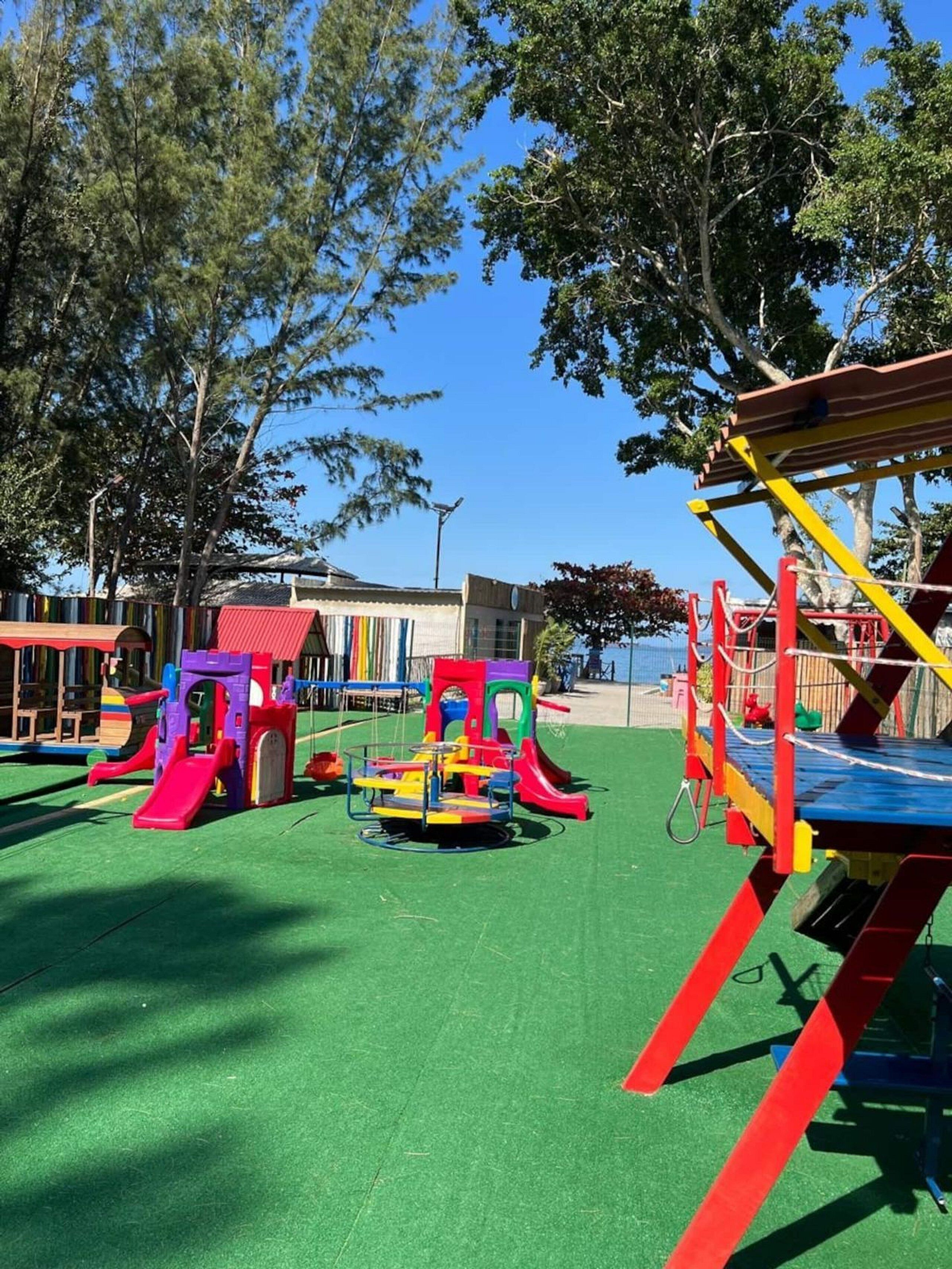 Um parquinho com diversas estruturas de recreação, um edifício ao fundo e árvores.