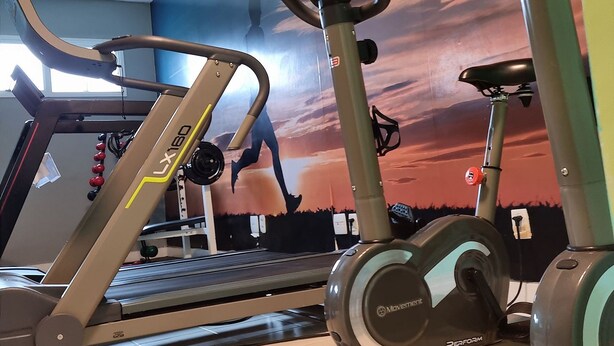 Ein Fitnessraum mit Ergometer, Laufband und Wandgemälde.
