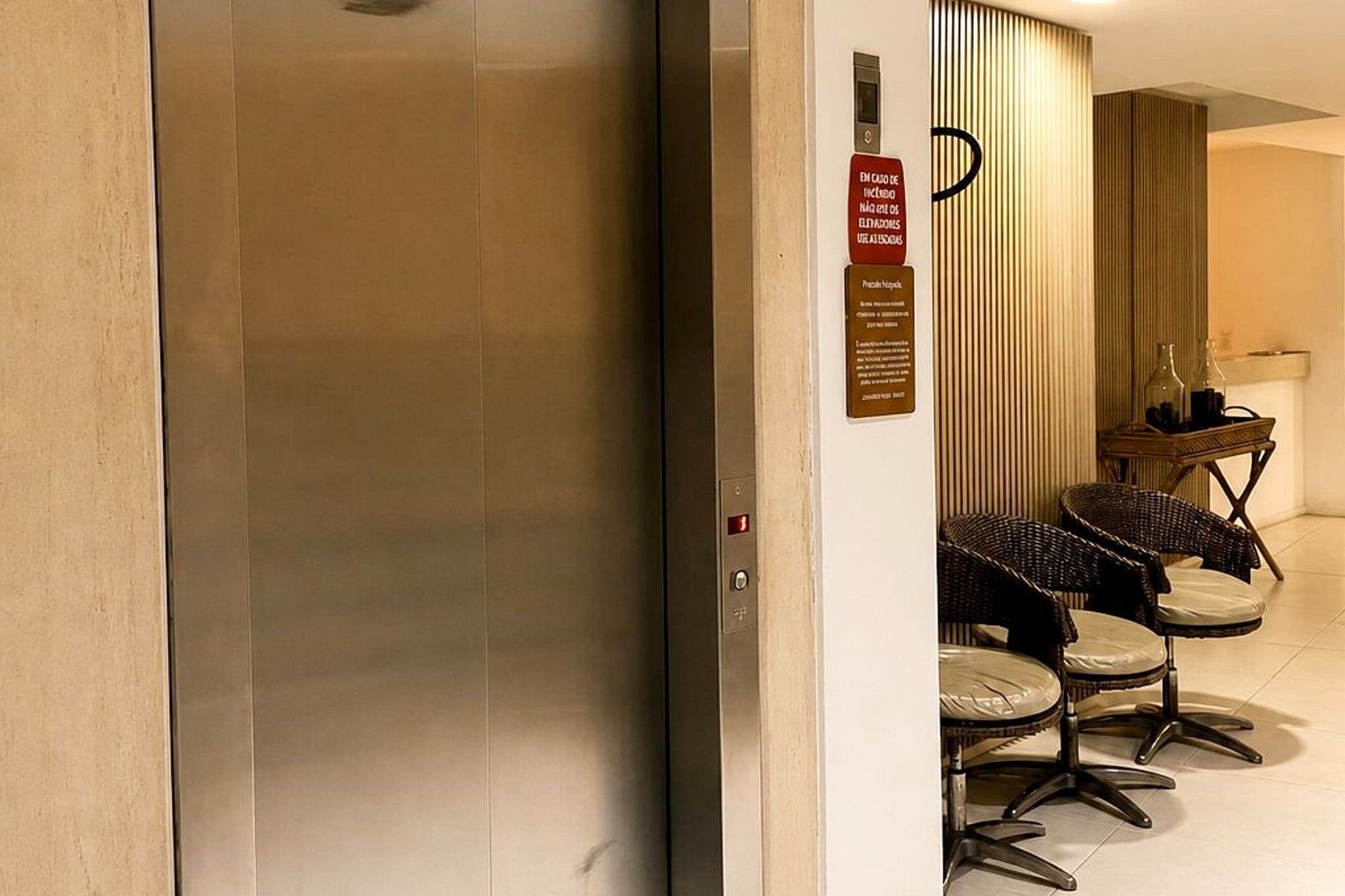 Uma área de recepção de hotel com elevador fechado, balcão de recepção e área de estar com cadeiras.