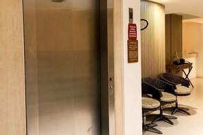 Ein Hotel-Empfangsbereich mit geschlossenem Aufzug, einem Empfangstresen und einer Sitzecke mit Stühlen.
