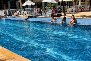 Une piscine où l’on voit des personnes dans l’eau, entourée de chaises longues et de parasols.