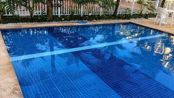 Piscina azul límpida com borda em azulejo e cerca branca ao fundo.