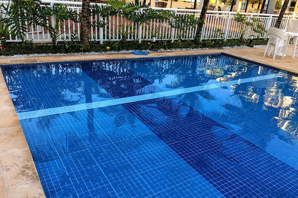 Una piscina azul cristalina con borde de azulejos y una valla blanca al fondo.