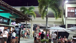 An outdoor dining area with tables and chairs, surrounded by buildings and palm trees. - Reserva do Sahy, Condado (Mangaratiba)