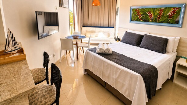 Une chambre d’hôtel avec un lit, un bureau et une chaise, une petite table, un téléviseur et un tableau au mur.