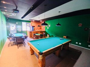 Una mesa de billar en una sala con paredes verdes, una zona de bar y un área de estar.