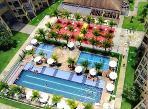 Vista aérea de un hotel con piscina, tumbonas y palmeras.