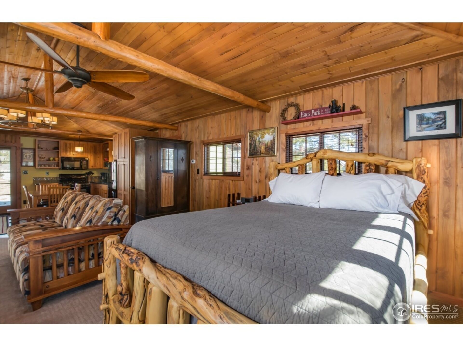 A wooden cabin interior with a bed, sofa, and kitchen area.