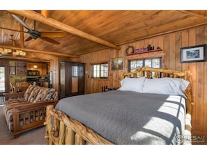 A wooden cabin interior with a bed, sofa, and kitchen area.