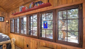 A cabin with large windows, wooden walls, and a bookshelf.