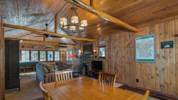 A wooden interior with a dining table, chairs, a fireplace, and a television.
