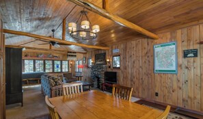 A wooden interior with a dining table, chairs, a fireplace, and a television.