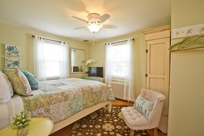 Une chambre à coucher comprenant un lit, une chaise, une commode, un miroir et un ventilateur de plafond.