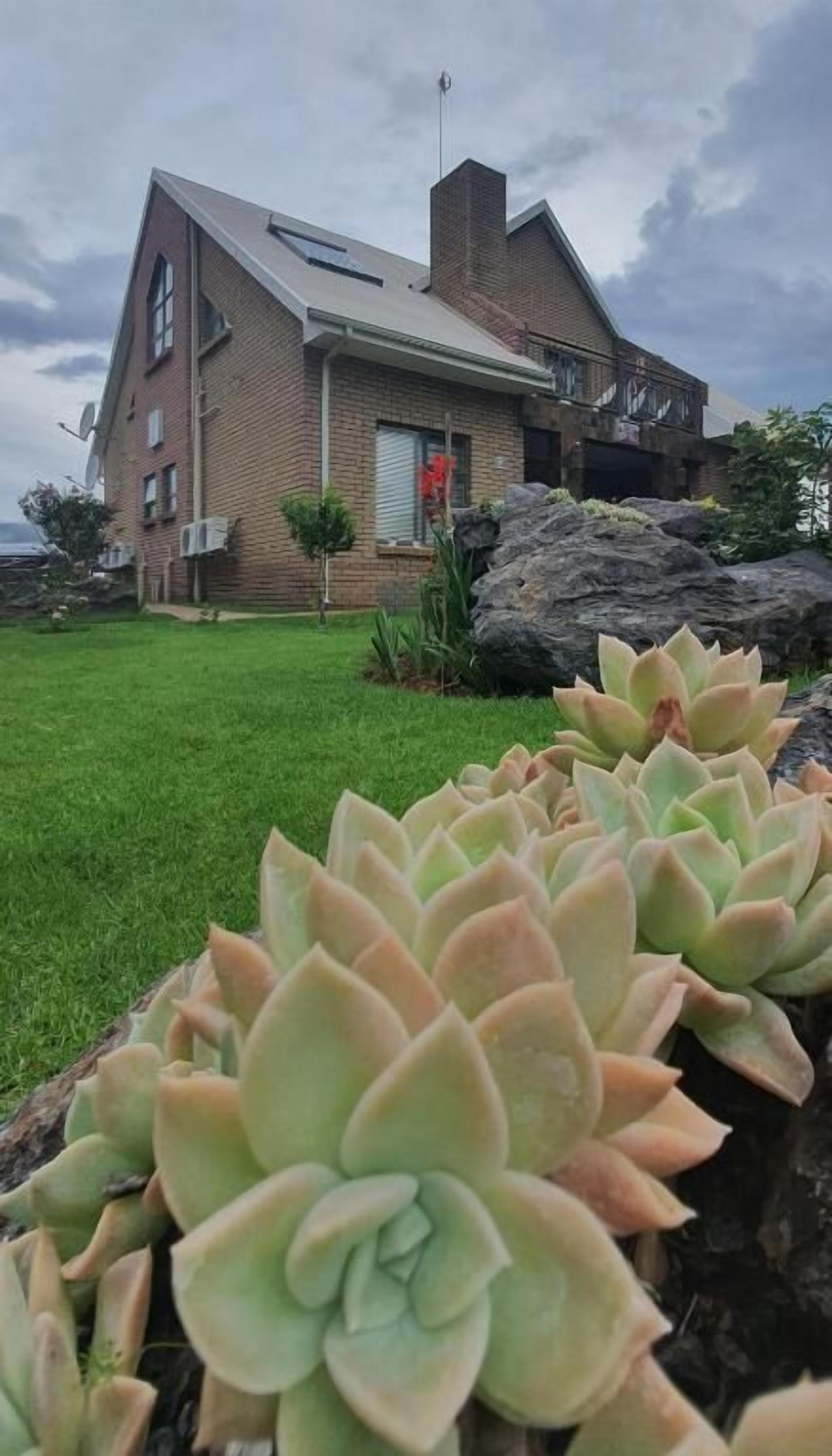 A brick house with a sloped roof, a small garden with succulents, and a large rock in the foreground.