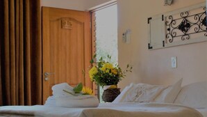 A bedroom with a bed, a wooden door, a wall-mounted artwork, and a window with curtains. - Eldorado Lodge CC (Kuruman)