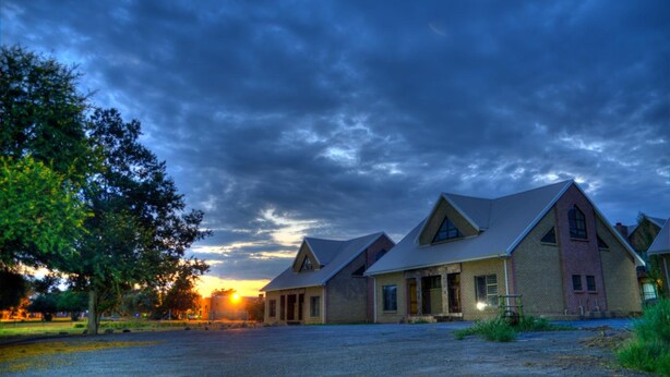 A row of brick buildings with pitched roofs, likely a hotel or residential complex, under a cloudy sky. - Eldorado Lodge CC (Kuruman)
