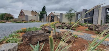Un edificio con diseño arquitectónico moderno, que presenta un camino de grava y un jardín ajardinado con rocas y cactus.