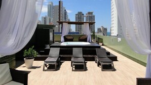 A rooftop terrace with a hot tub, lounge chairs, and a view of high-rise buildings. - Hotel das Américas (Balneário Camboriú)