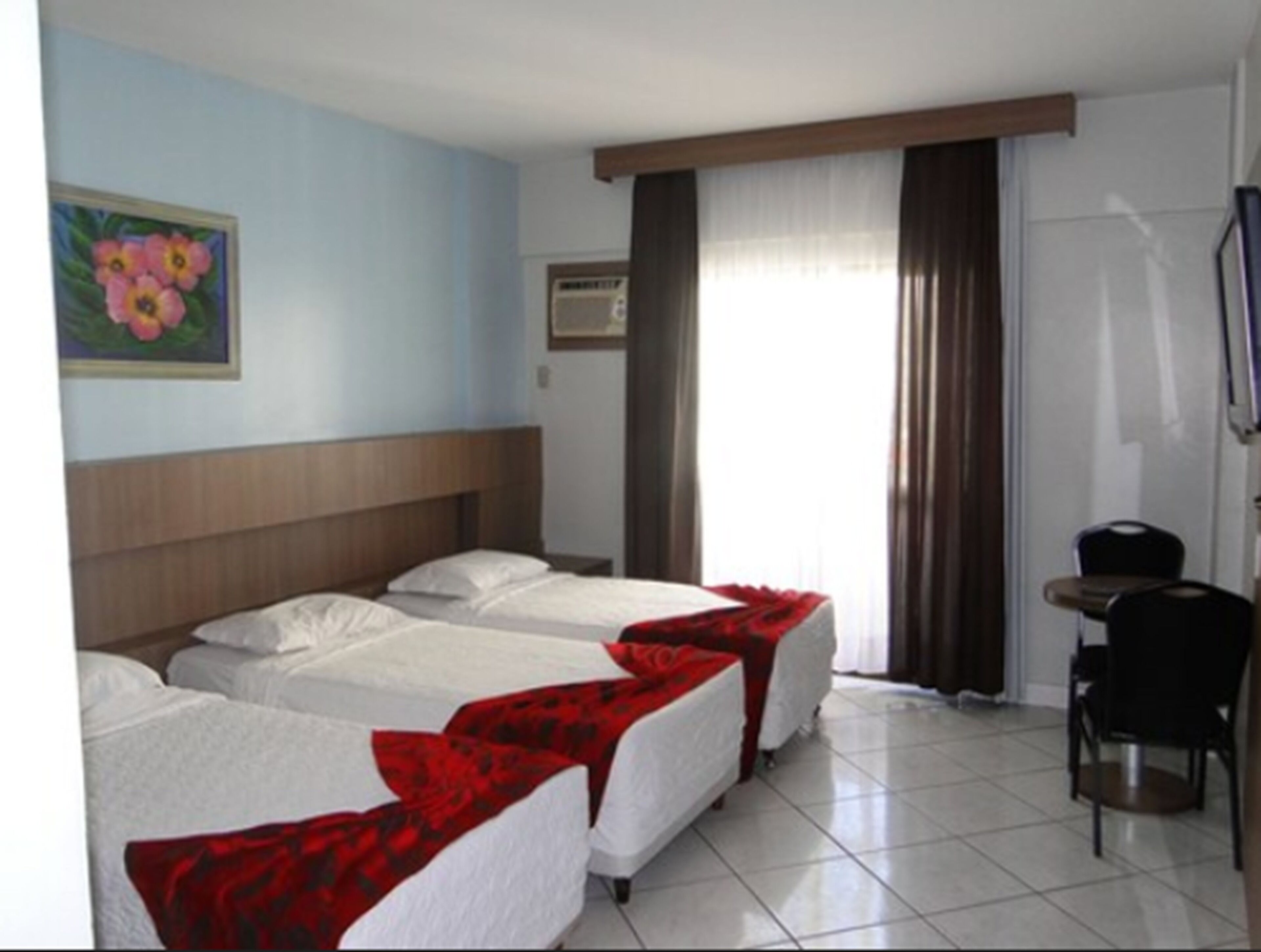 Habitación de hotel con dos camas individuales, una mesita, una silla, un cuadro en la pared y una ventana con cortinas.