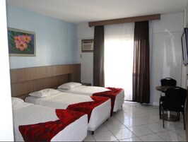 Habitación de hotel con dos camas individuales, una mesita, una silla, un cuadro en la pared y una ventana con cortinas.