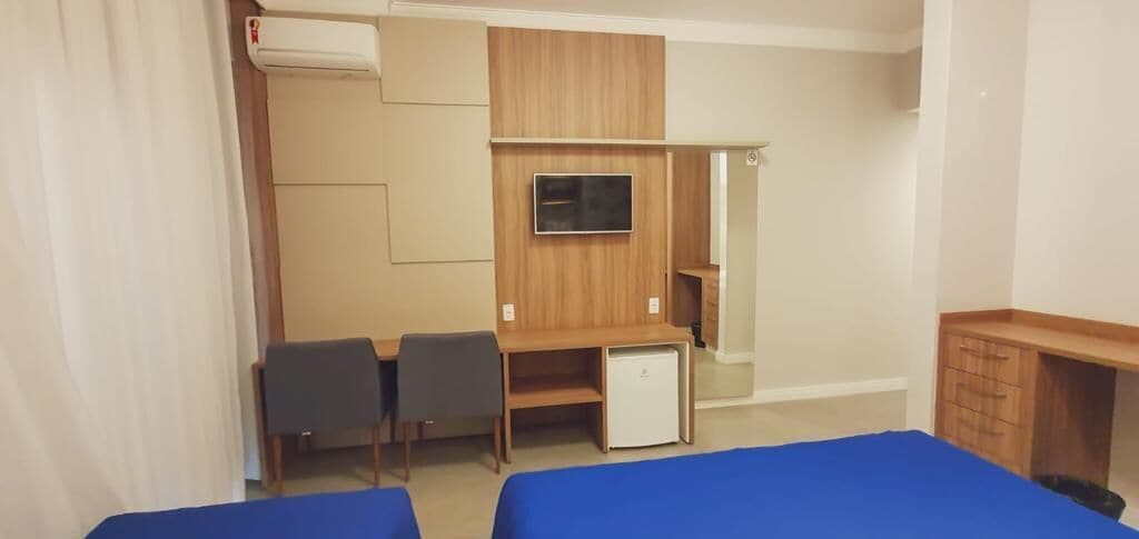 A hotel room with two beds, a desk with a chair, a television, and a small refrigerator.