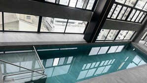 An indoor swimming pool with clear glass walls, a metal ladder, and a view of surrounding buildings. - Hotel das Américas (Balneário Camboriú)