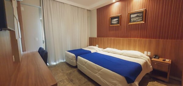 A hotel room with two beds, a wooden headboard, a desk, and a chair.