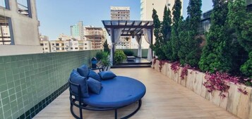 A rooftop terrace with a blue sofa, a pergola, and a view of the cityscape.