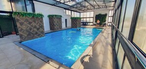 Una piscina interior con agua azul cristalina, rodeada de paredes con diseños geométricos y plantas verdes.