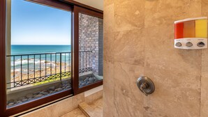 Une salle de bain avec douche, vue sur la plage et mur en pierre.